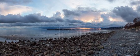 Photo for Rocky Beach and White Rock Pier on the West Coast of Pacific Ocean. Dramatic Cloudy Sunset Sky. Vancouver, British Columbia, Canada. Panorama - Royalty Free Image