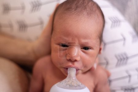 Téléchargez les photos : Adorable nouveau-né garçon assis sur les genoux de la mère Nourrir du lait à partir d'une bouteille - en image libre de droit