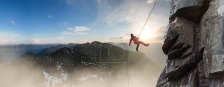Photo for Adventure Man on rope Rappelling down a mountain cliff. Extreme Sport Composite. Aerial landscape from British Columbia, Canada. Sunset - Royalty Free Image