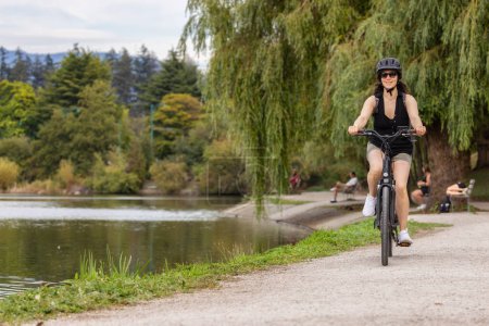 Téléchargez les photos : Femme caucasienne en forme faisant du vélo électrique sur une piste dans Stanley Park, Downtown Vancouver, Colombie-Britannique, Canada. - en image libre de droit