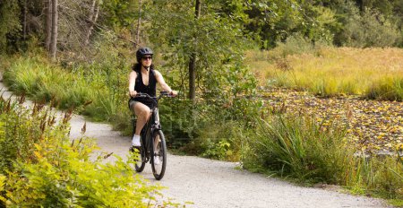 Photo for Fit Caucasian Woman riding an Electric Bicycle on a trail in Stanley Park, Downtown Vancouver, British Columbia, Canada. - Royalty Free Image