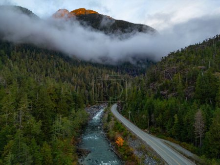 Foto de Scenic Highway by Trees and River with Mountains in Background (en inglés). Colorido amanecer. Isla de Vancouver, Columbia Británica, Canadá. - Imagen libre de derechos
