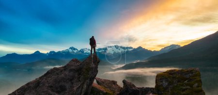 Téléchargez les photos : Epic Adventure Composite of Man Randonneur au sommet d'une montagne rocheuse. Coucher de soleil spectaculaire. 3d Crête de rendu. Paysage de fond d'Amérique du Nord. Concept de liberté. - en image libre de droit