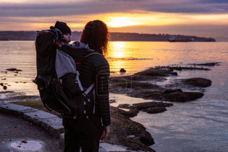 Photo for Mother with Baby in Carrier on Seawall in Stanley Park. Sunset, Fall Season. Downtown Vancouver, British Columbia, Canada. - Royalty Free Image