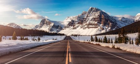 Road with Canadian Rocky Mountain Peaks Covered in Snow. Ciel levant coloré. Banff, Alberta, Canada.