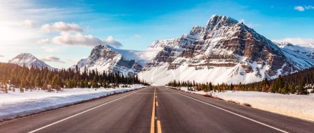 Téléchargez les photos : Road with Canadian Rocky Mountain Peaks Covered in Snow. Ciel levant coloré. Banff, Alberta, Canada. - en image libre de droit