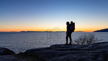 Mother and Baby Boy in backpack carrier hiking on Rocky ocean coast. Lighthouse park, West Vancouver, BC, Canada.