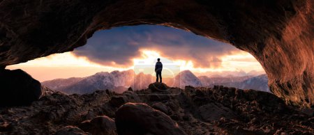 Foto de Hombre aventurero excursionista de pie en una cueva. Niebla y montañas en el fondo. Aventura compuesto 3d renderizado. Imagen aérea del paisaje de BC, Canadá. Puesta de sol cielo nublado - Imagen libre de derechos