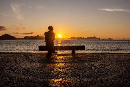 Foto de Hermosa vista al amanecer a la estatua del poeta sentado en el banco de la playa en Copacabana, Río de Janeiro, Brasil - Imagen libre de derechos