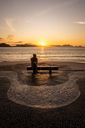 Téléchargez les photos : Belle vue du lever du soleil sur une statue de poète assise sur un banc de plage à Copacabana, Rio de Janeiro, Brésil - en image libre de droit