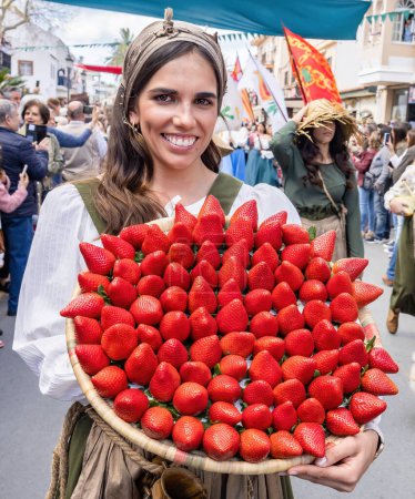 Photo for Huelva,Spain-March 18, 2023:A huge plate with big strawberries, variety Freson de Palos, in the hand of a young woman parading in the Medieval Discovery Fair in Palos de la Frontera, Huelva, Andalusia - Royalty Free Image