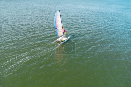 Aerial drone view of a catamaran sailboat sailing in the Turquoise Color waters of El Portil beach, with a multicolor sail, in Punta Umbria Municipality, Huelva province, Andalusia, Spain
