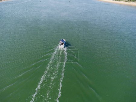 Drohnenaufnahme eines Motorbootes, das im Fluss Piedras zwischen dem Stranddorf El Portil und der Sandbank La Flecha navigiert