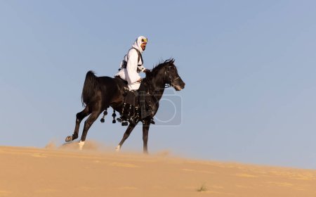 Téléchargez les photos : Arabe saoudien chevauchant son étalon noir dans un désert - en image libre de droit