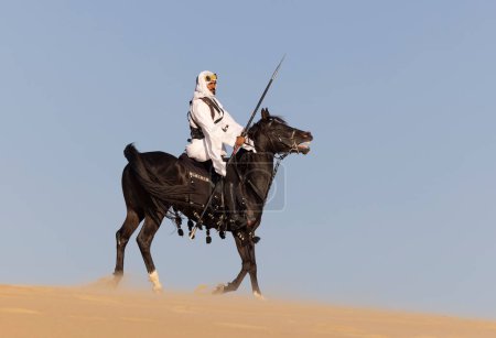 Photo for Saudi arabian man riding on his black stallion in a desert - Royalty Free Image