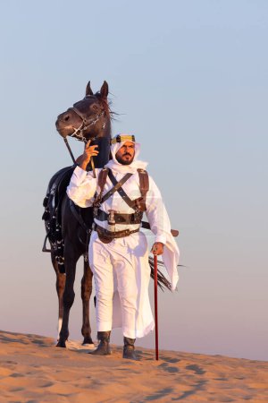 Photo for Saudi man in a desert with his black horse - Royalty Free Image