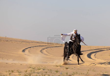 Téléchargez les photos : Saoudien en vêtements traditionnels dans le deset chevauchant un cheval noir - en image libre de droit