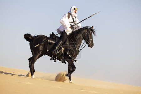 Foto de Hombre saudí con ropa tradicional en el deset montando un caballo negro - Imagen libre de derechos