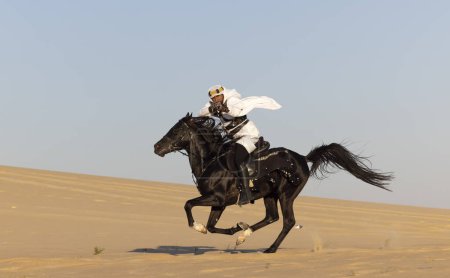 Foto de Hombre saudí en un desierto, montando un semental negro, disparando un rifle de caza - Imagen libre de derechos