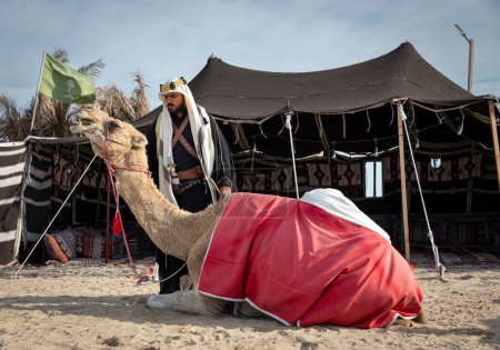 Foto de Hombre beduino con su halcón y camello descansando frente a su tienda - Imagen libre de derechos