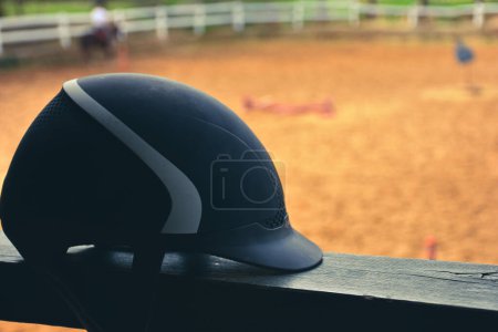 Téléchargez les photos : Close up view of  black Equestrian helmet with blurred horse farm view. Isolated Horse riding hat on the railing in the horse farm. - en image libre de droit