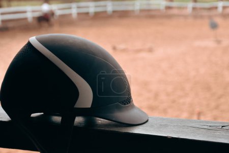 Téléchargez les photos : Close up view of  black Equestrian helmet with blurred horse farm view. Isolated Horse riding hat on the railing in the horse farm. - en image libre de droit