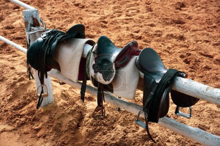 Foto de Monturas de caballo y frenos de pie en la valla en la granja de caballos en la pista de entrenamiento - Imagen libre de derechos