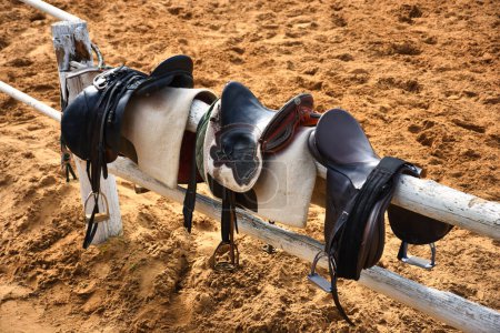 Téléchargez les photos : Horse saddles and bridles standing on fence at horse farm on training track - en image libre de droit