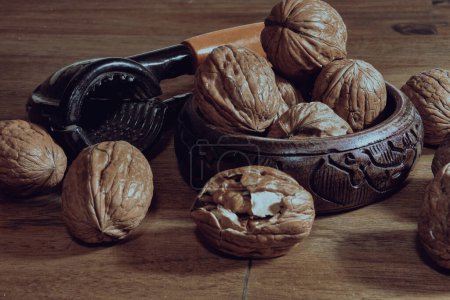 Photo for Heaps of walnuts waiting to be cracked in a wooden bowl on a wooden table with a walnut cracker next to it. A walnut is cracked and its inside is visible. Organic healthy eating - Royalty Free Image