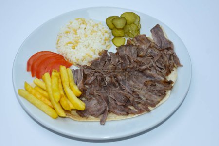 Foto de Vista superior de Iskender doner kebab con arroz, papas fritas, tomates y pepinos en escabeche servidos en un plato blanco - Imagen libre de derechos
