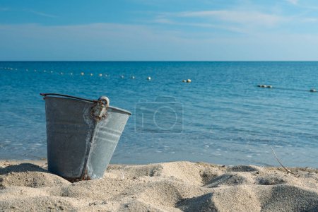 An empty beach metal bucket or bin on the beach among sands. 1960's summer concept. Water pollution
