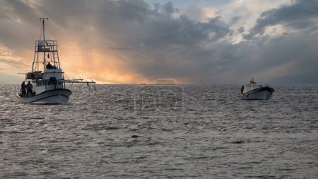 Téléchargez les photos : Un petit bateau de pêche et un bateau d'espadon revenant de la mer à Gokceada, Imbros - en image libre de droit