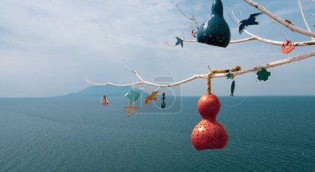 Photo for Decorative pumpkin lamps hanging on tree branches against the North Aegean sea. Samothrace island in the background. Calabash lamp interior decoration is made of dry pumpkins - Royalty Free Image