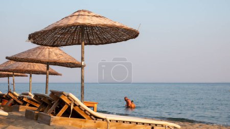 Téléchargez les photos : Chaises longues et parasols vides au coucher du soleil sur la plage de Gkeada Aydincik (Kefalos). anakkale Turquie - en image libre de droit