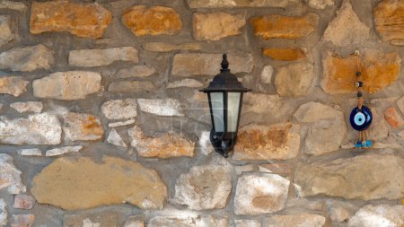 Foto de Una lámpara de linterna montada en una pared de piedra y una perla turca junto a ella. Decoración de pared jardín. - Imagen libre de derechos