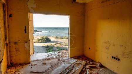 Foto de Vista de la costa a través de la ventana rota en una habitación de edificio de hotel abandonado y demolido. Vista a través de una ventana rota al mar. - Imagen libre de derechos