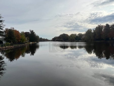 Photo for View of the Brainerd Lake in autumn in Cranbury, New Jersey, United States. Autumn landscape with lake, trees and cloudy sky reflected in water - Royalty Free Image