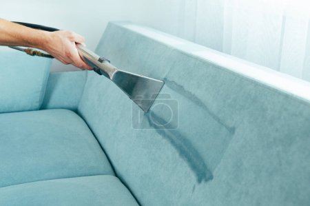 Reinigungskonzept. Mann putzt Cyan-Sofa im Zimmer Virenprävention, die im Inneren desinfiziert. Prozess der Tiefenreinigung von Möbeln. Professionelle chemische Reinigung. Kleinunternehmerdarlehen