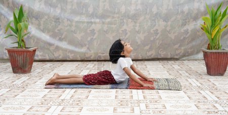 Téléchargez les photos : Petite fille attrayante faisant de l'exercice, enfant asiatique pratiquant la méditation à l'intérieur, Yoga et mode de vie sain concept - en image libre de droit