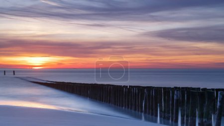 Téléchargez les photos : Coucher de soleil sur la côte de Vlissingen Hollande avec les poteaux en bois - en image libre de droit