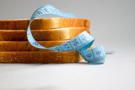 Téléchargez les photos : Piece of white bread measuring tape on a light background - en image libre de droit