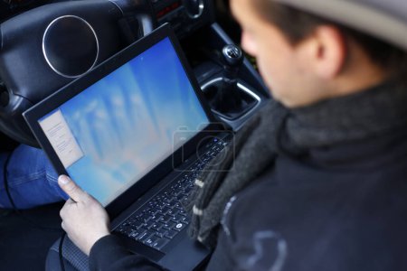 Téléchargez les photos : Un mécanicien automobile inspectant une voiture à l'aide d'un dispositif de diagnostic électronique - en image libre de droit