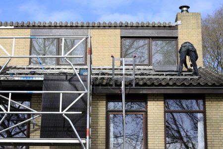 Téléchargez les photos : Ingénieurs de service installant des panneaux solaires sur le toit d'une maison résidentielle - en image libre de droit