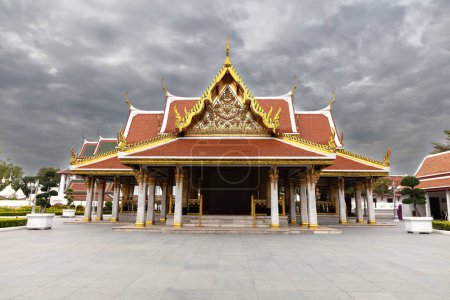 Königlicher Pavillon (Mahajetsadabadin) in Bangkok, Thailand. Rotes Ziegeldach mit weißem und goldenem Zierstreifen. Dunkler wolkenverhangener Himmel. 