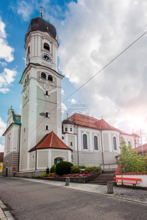 North-side wide angle view of the St. Andreas Church in Nesselwang / Bavaria from in front of a blue sky with large white clouds with lens flares in the summer of 2023.