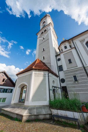 Photo for Nesselwang, Germany - July 06, 2023: Wide angle north view of the Saint Andreas Church with bell tower and tower chapel in front of a blue sky with clouds. - Royalty Free Image