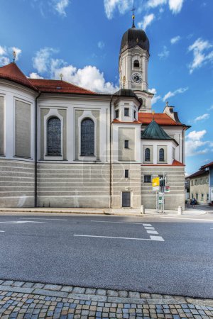 Photo for Nesselwang, Germany - July 06, 2023: South facade of the Saint Andreas Church with signposts and a view over the main street against a blue sky with clouds. - Royalty Free Image