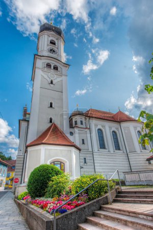 Photo for Nesselwang, Germany - July 06, 2023: Wide angle north view of Saint Andreas Church with bell tower and flower beds in front of a blue sky with clouds. - Royalty Free Image
