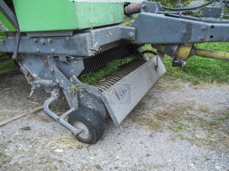 Partial view of the PTO spring tines and pickup roller of a baler on a gravel surface after intensive use.