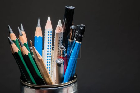 Kleine Auswahl an Bleistiften, die senkrecht in einer Blechdose vor dunklem Hintergrund stehen.